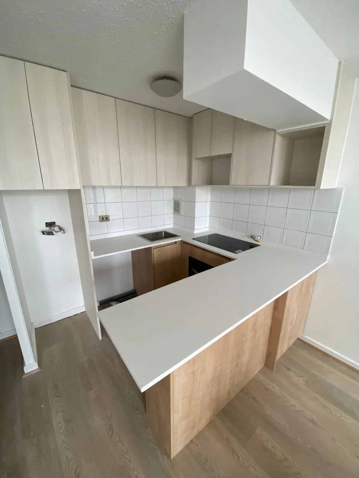 Cocina terminada, con la barra de cubierta blanca y los muebles claros hasta el cielo