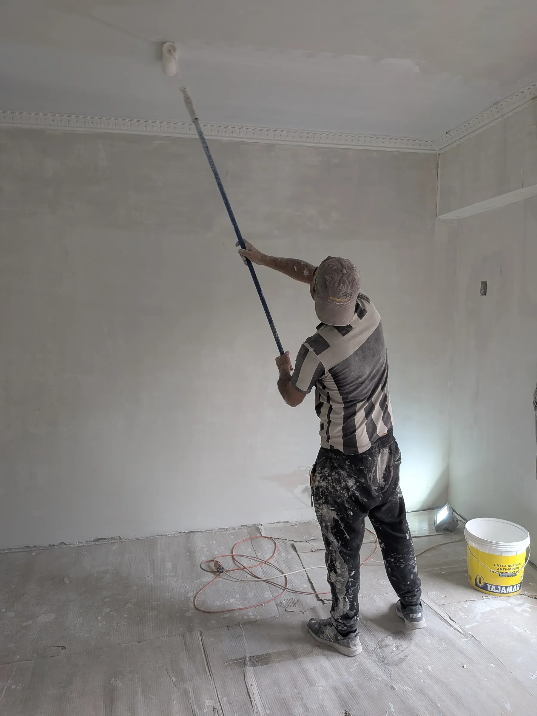 Maestro pintando un muro con rodillo de extensión en una vivienda en obra